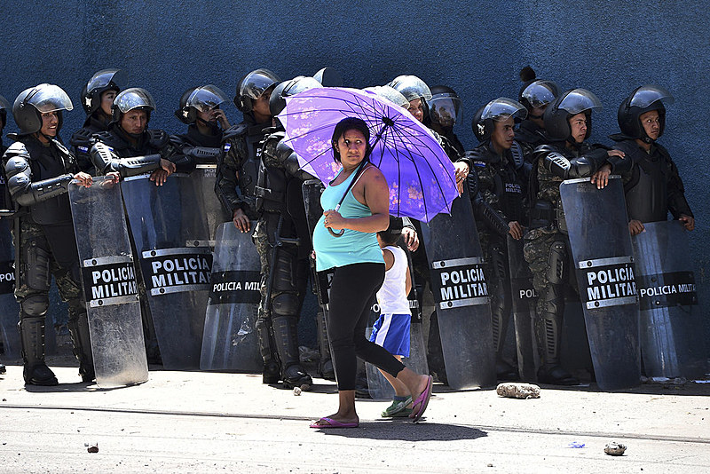 Uma mulher e uma criança atravessam a rua em meio à repressão da polícia contra estudantes nesta segunda (24) na capital de Honduras