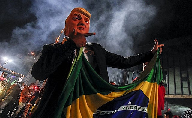 A Trump doll holds the Brazilian flag and does Jair Bolsonaro’s signature “guns up” hand gesture