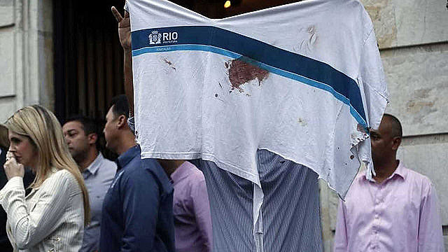 Protester holds Marcos Vinícius’ school uniform with blood stain; 14-year-old student is yet another victim of police operations in Rio