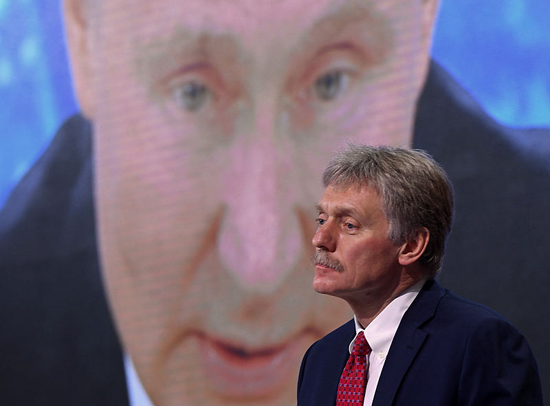 O porta-voz do Kremlin, Dmitry Peskov, em frente a uma tela que exibe o presidente russo, Vladimir Putin, discursando em sua coletiva de imprensa anual.