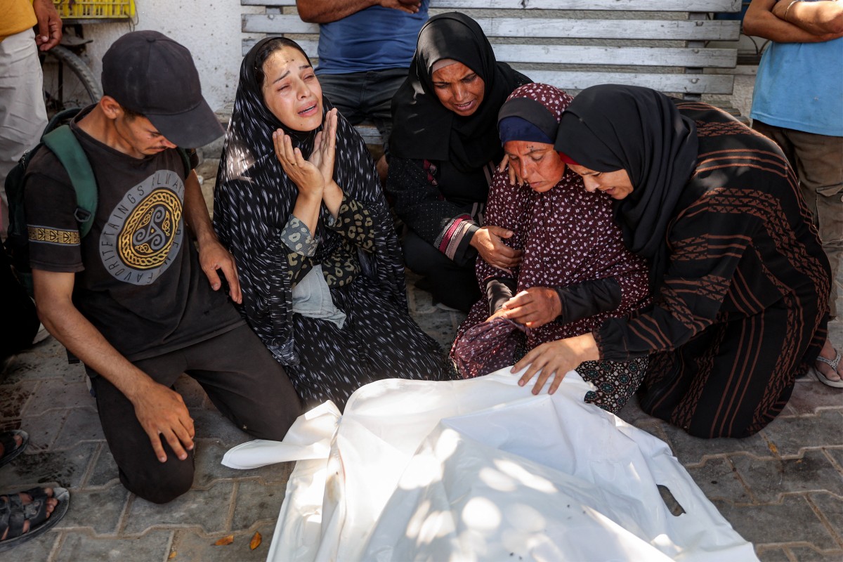Mulheres choram ao lado do corpo de vítima de ataque israelense às filas de ajuda humanitária no hospital Al-Shifa, em Gaza, em 14 de junho de 2025