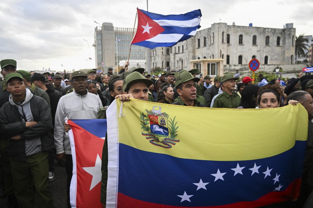 Membros das Forças Armadas seguram bandeiras venezuelanas e cubanas durante um protesto “anti‑imperialista” em frente à Embaixada dos EUA contra a incursão dos EUA na Venezuela, onde 32 soldados cubanos perderam a vida, em Havana, em 16 de janeiro de 2026.