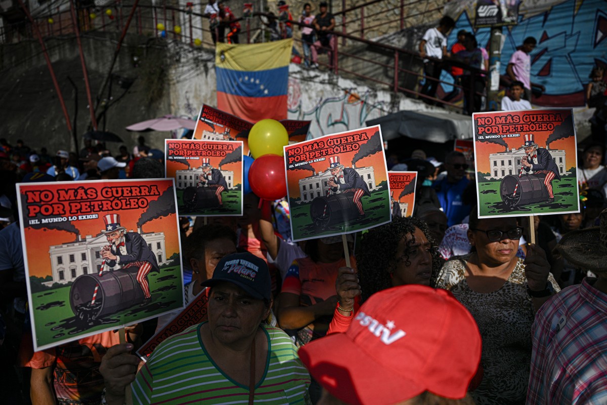 Apoiadores do presidente venezuelano Nicolás Maduro exibem cartazes com os dizeres em espanhol "Chega de guerra pelo petróleo, o mundo exige isso", durante um protesto contra a atividade militar dos EUA no Caribe, na comunidade de San José, no bairro de Petare, em Caracas, em 13 de dezembro de 2025.