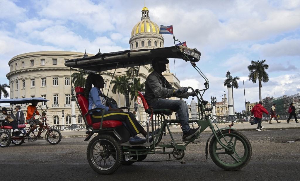 Um táxi triciclo decorado com a bandeira cubana passa próximo ao Capitólio em Havana em 30 de janeiro de 2026. O presidente cubano, Miguel Díaz-Canel, em 30 de janeiro de 2026, denunciou a tentativa do presidente dos EUA, Donald Trump, de “asfixiar” a economia da ilha comunista sob um “falso pretexto”.
