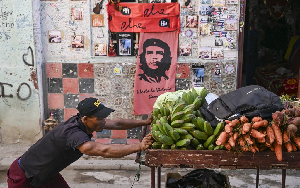 Um vendedor ambulante empurra um carrinho carregado de bananas, cenouras e beterrabas em frente a uma loja de souvenirs que exibe imagens do guerrilheiro cubano nascido na Argentina, Ernesto Che Guevara, em Havana, Cuba, em 5 de fevereiro de 2026.