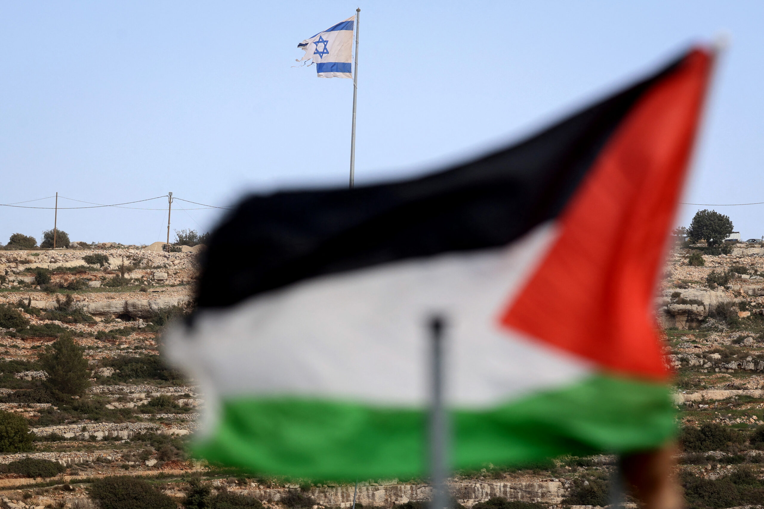 Bandeira palestina e outra israelense no topo de uma colina com vista para a Vila de Umm Safa, ao norte de Ramallah, na Cisjordânia ocupada.
