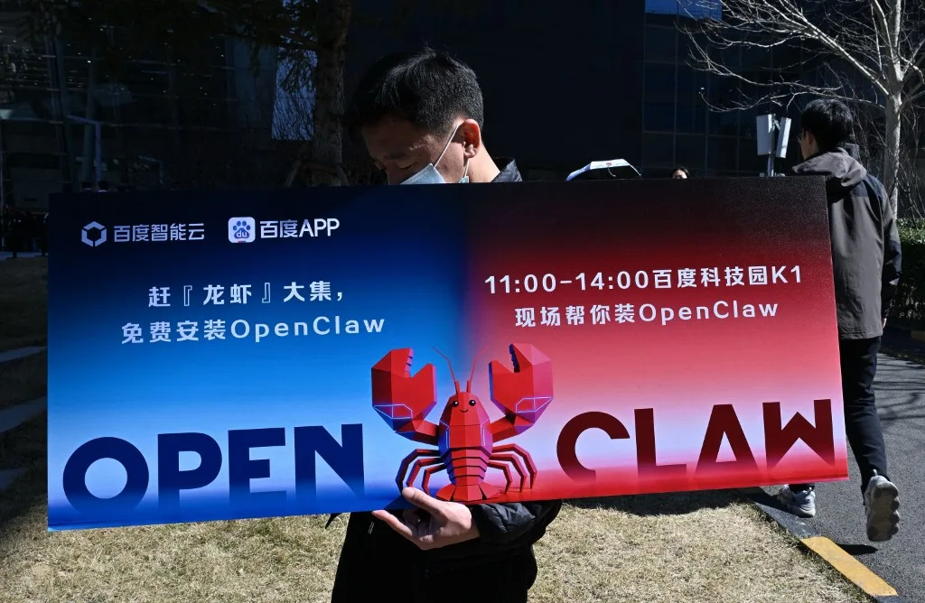 Um homem segura um cartaz com a imagem do OpenClaw, um assistente de IA de código aberto, durante um evento na sede da Baidu em Pequim, em 11 de março de 2026.
