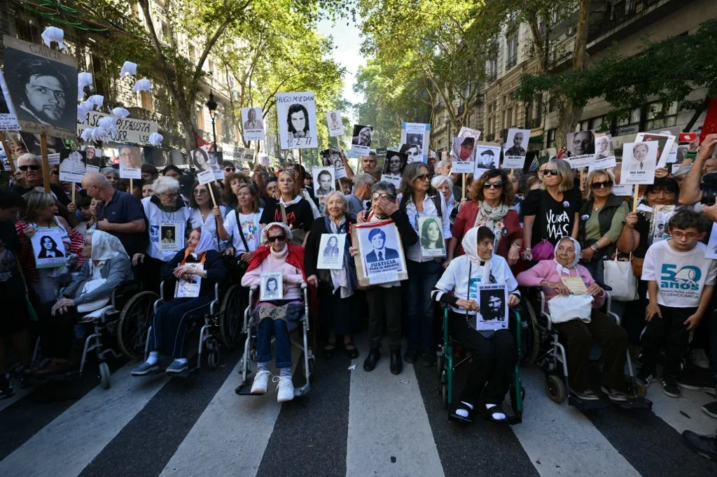 Membros da associação de direitos humanos Madres de Plaza de Mayo seguram os retratos de seus filhos e filhas desaparecidos enquanto chegam à Praça de Maio no 50º aniversário do início da última ditadura militar (1976–1983) em Buenos Aires, em 24 de março de 2026.
