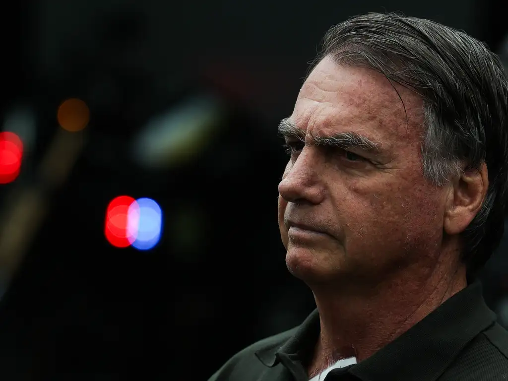 Imagem mostra rosto de Jair Bolsonaro em foco, sério, olhando para o horizonte.