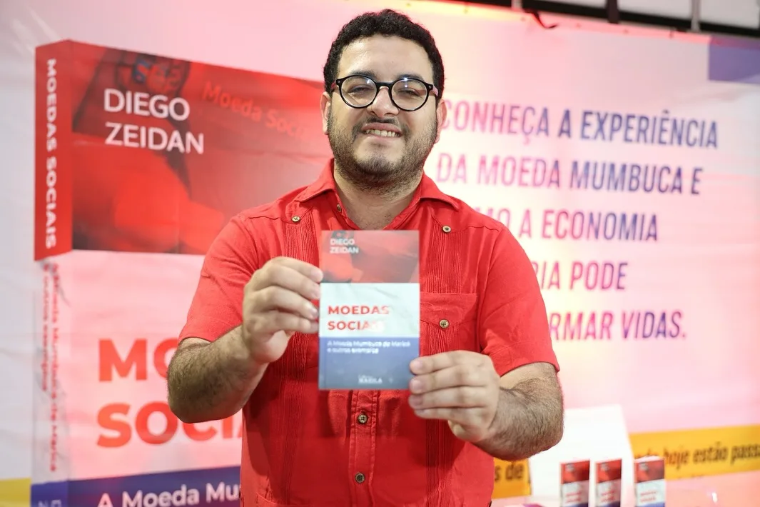 Diego Zeidan posa para foto com o folder do livro de sua autoria "moedas sociais"