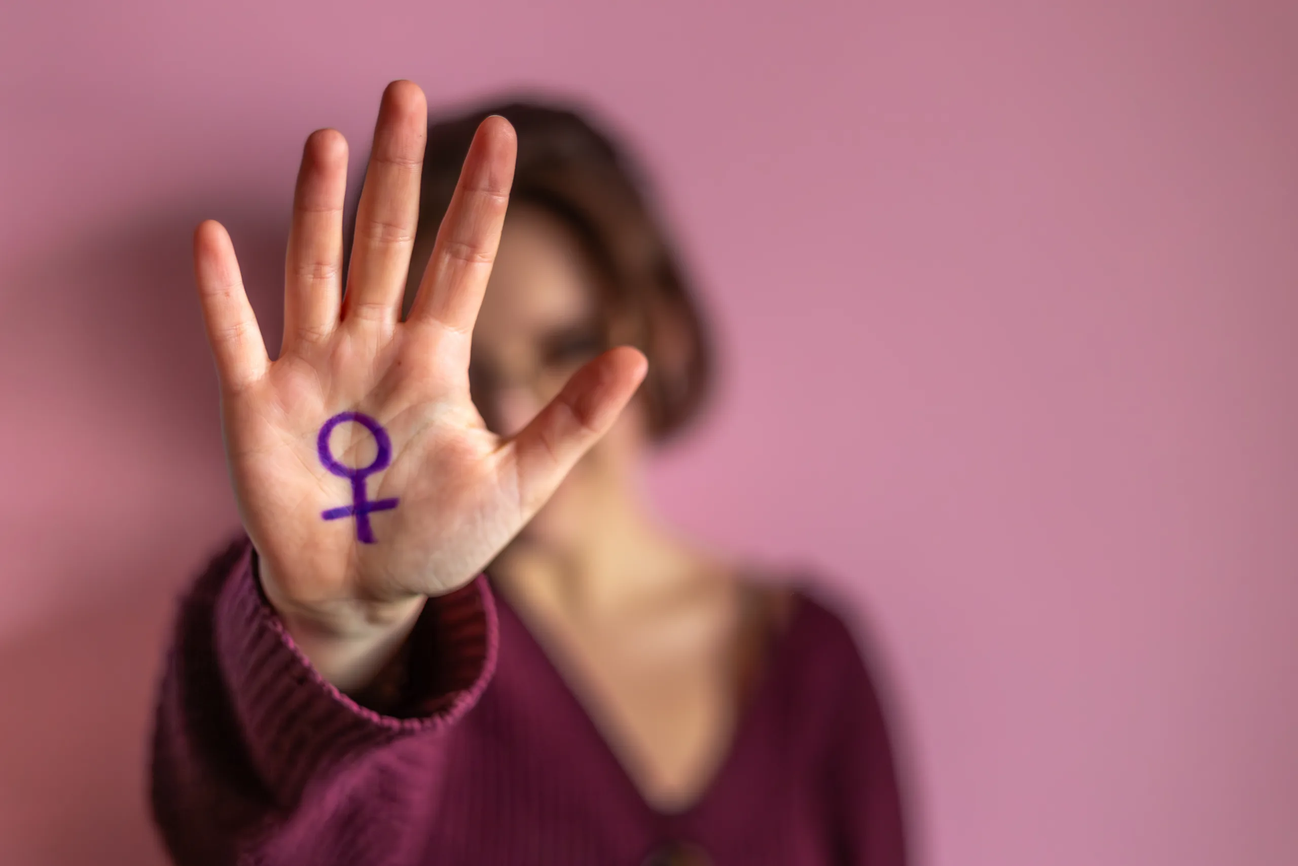 Mulher faz sinal de pare com a mão. Em sua palma está desenhado o espelho de vênus, símbolo do feminismo