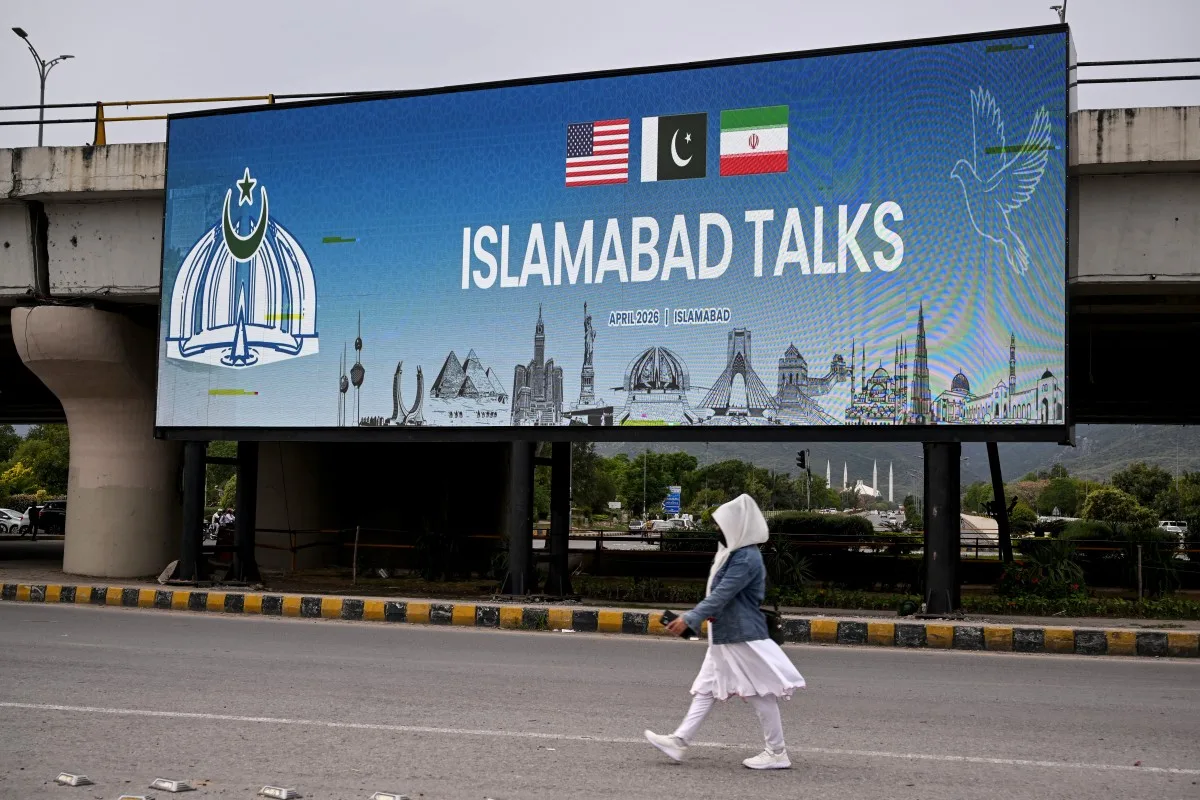 Mulher caminha ao lado de uma tela digital que exibe notícias sobre as negociações de paz entre os EUA e o Irã, em uma rua de Islamabad, em 10 de abril de 2026