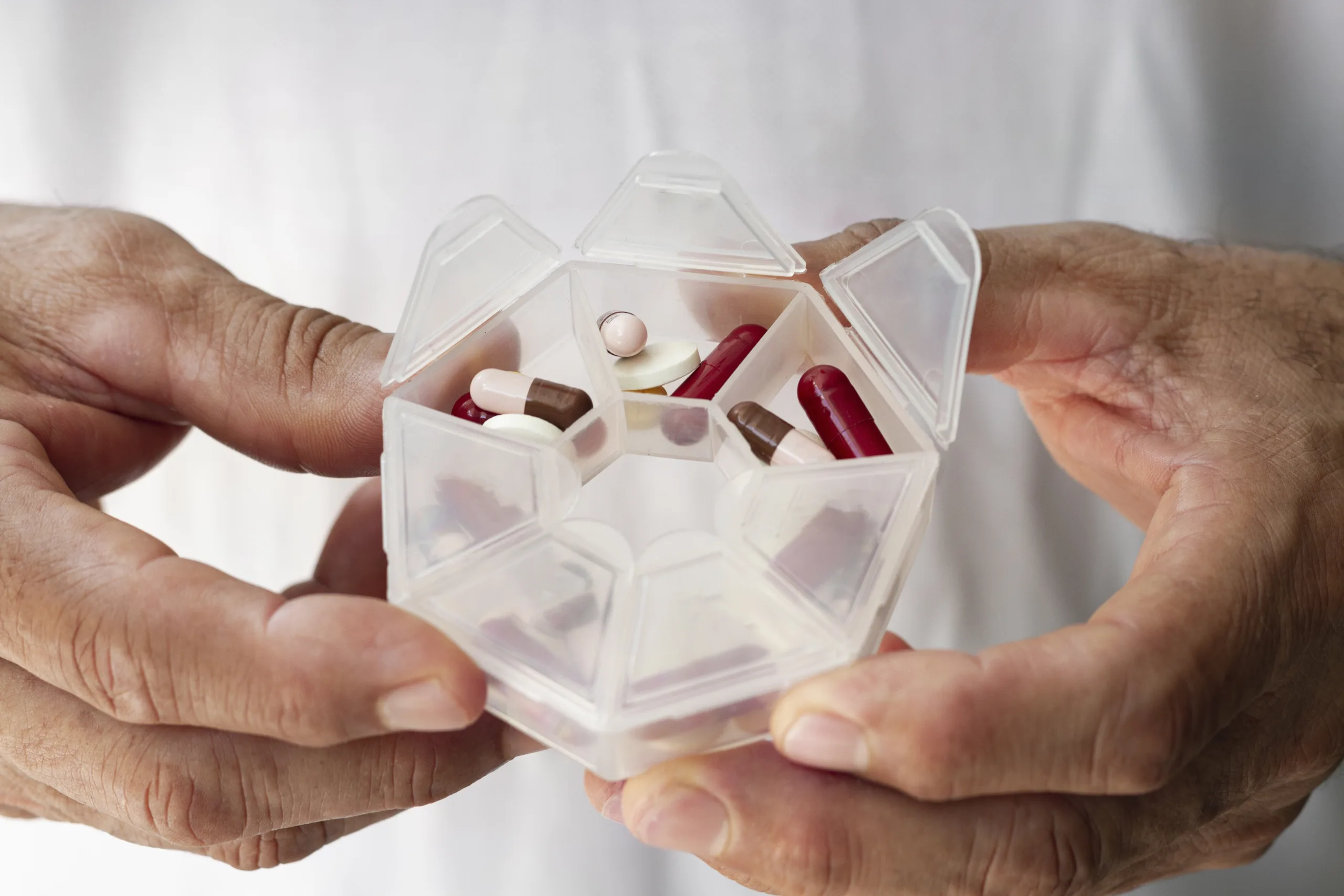 Imagem mostra mão humana segurando caixa de medicamentos em pílulas distribuídas em divisórias plásticas