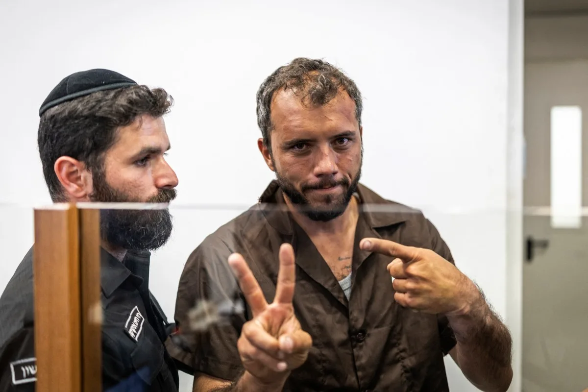 Thiago Ávila acena um "V" de vitória enquanto é levado para depor um prisão de Israel