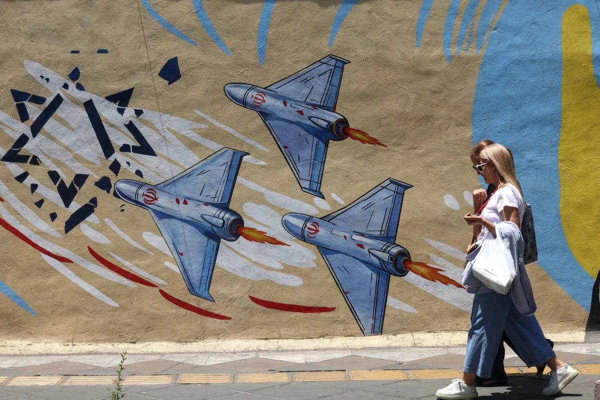 Mulheres iranianas caminham em frente a um mural anti-EUA e anti-Israel em Teerã, em 3 de junho de 2026.